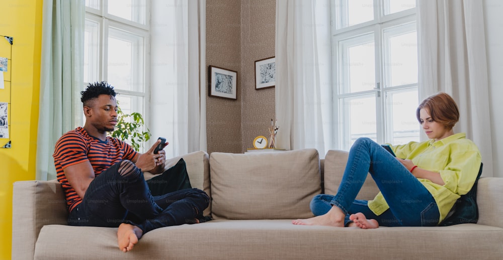Junges gemischtes Paar, süchtig nach Smartphones, das zu Hause auf einem Sofa sitzt.