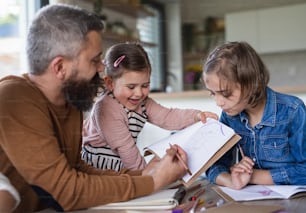 A father with daughters indoors at home, drawing pictures.