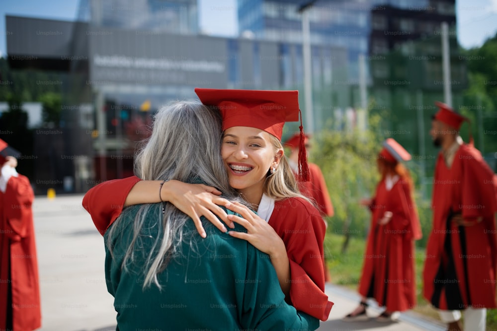 A portrait of cheerful university student hugging mother outdoors, graduation concept.