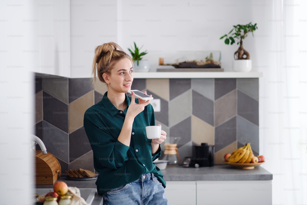 A portrait of young woman student with coffee at home, using smartphone.