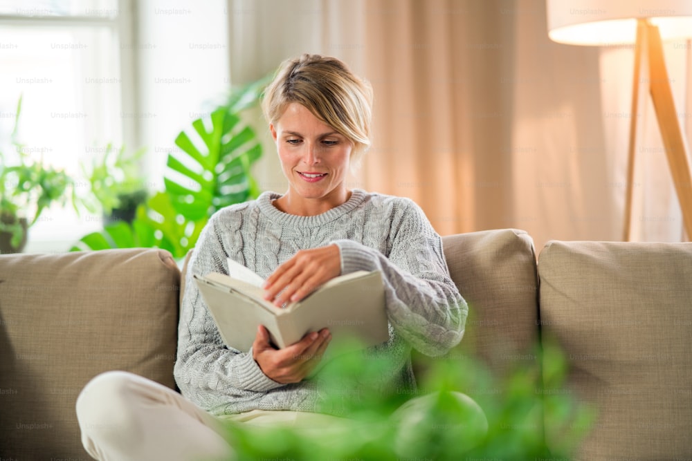 Front view portrait of woman relaxing and reading book indoors at home, mental health care concept.