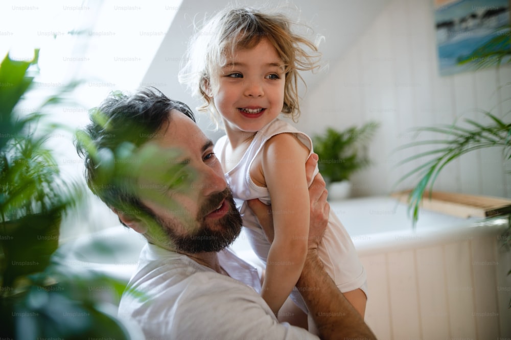 Mature father with a small daughter indoors in bathroom at home.
