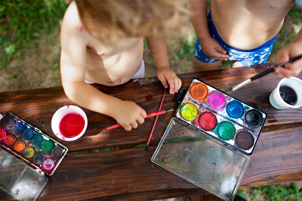 Sección media de niño y niña irreconocibles pintando al aire libre en verano.
