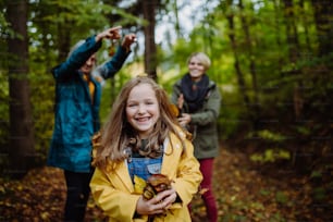 A happy little girl with mother and grandmother having fun with leaves during autumn walk in forest