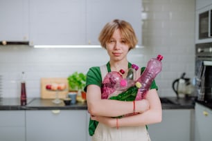 A teenage girl holding empty plastic bottles in kitchen and looking at camera.