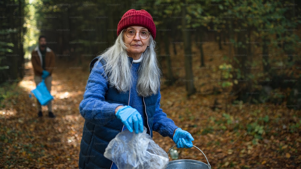 Una voluntaria mayor mirando a la cámara y limpiando el bosque de desechos, concepto de servicio comunitario