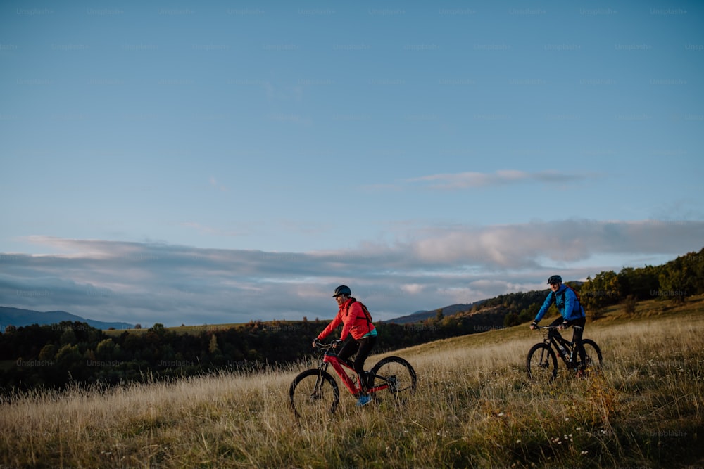 Una vista lateral de una pareja mayor activa montando en bicicleta al aire libre en el campo en el día de otoño.