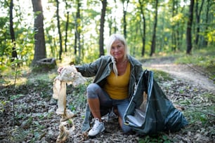 A senior woman ecologist picking up waste outdoors in forest.