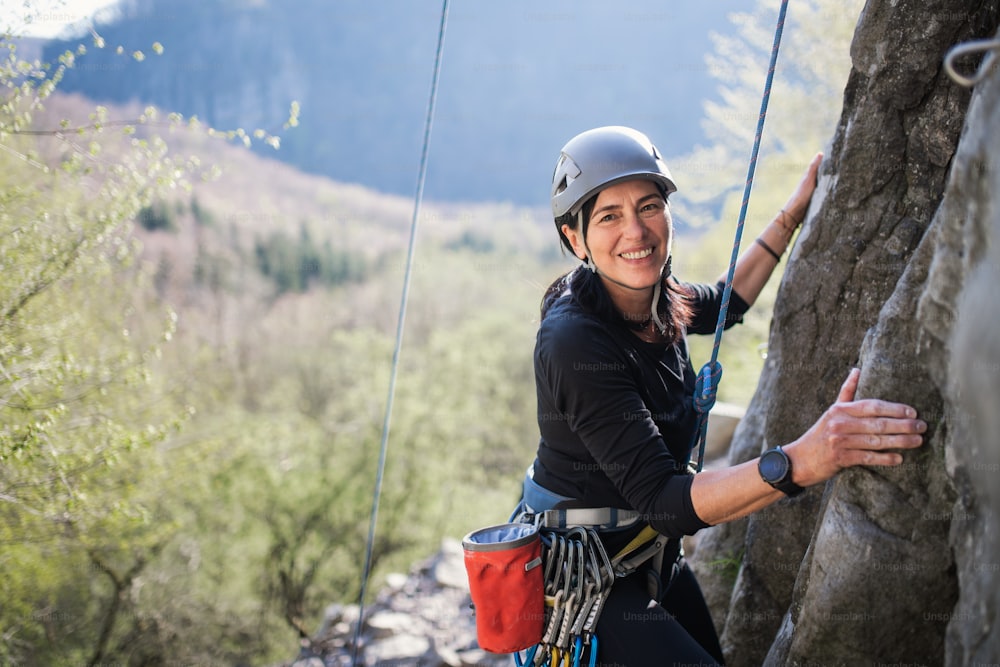 Retrato da mulher sênior escalando rochas eolhando para a câmera ao ar livre na natureza, estilo de vida ativo.