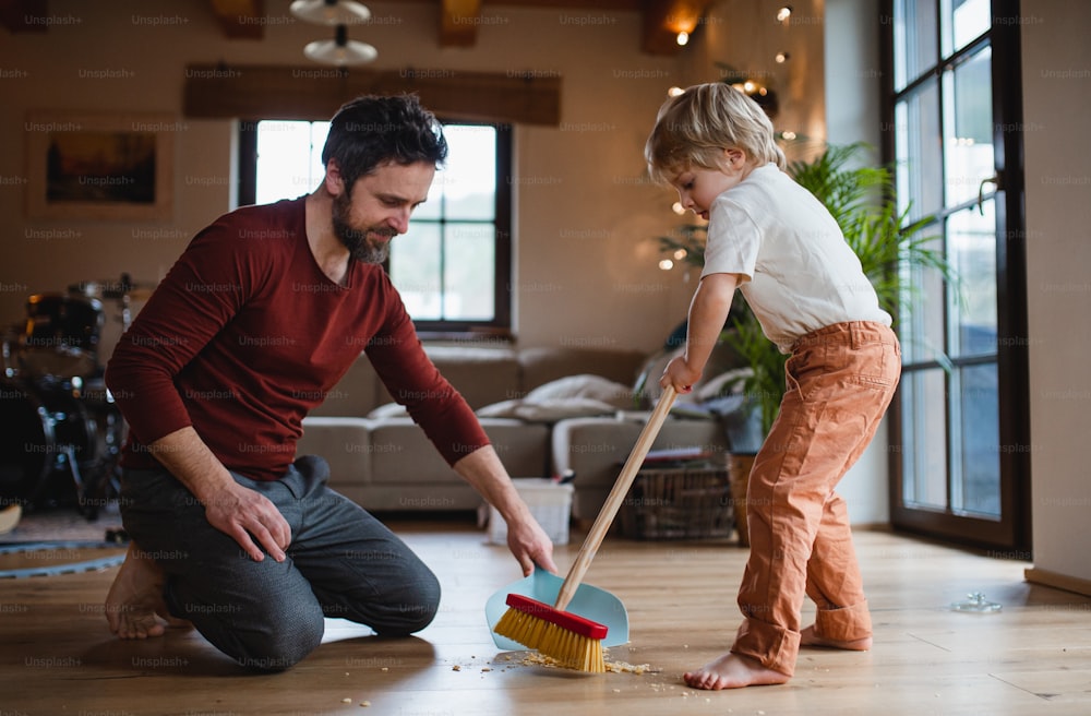 小さな息子が家で掃除をしている父親、毎日の家事のコンセプト。
