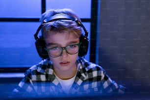 A young gamer boy with headphones playing computer video game.
