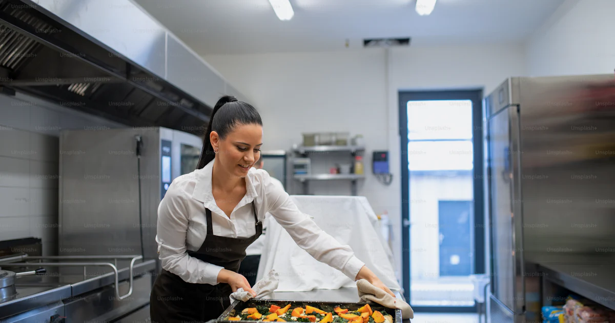 A professional chef working on her dishes indoors in restaurant kitchen ...