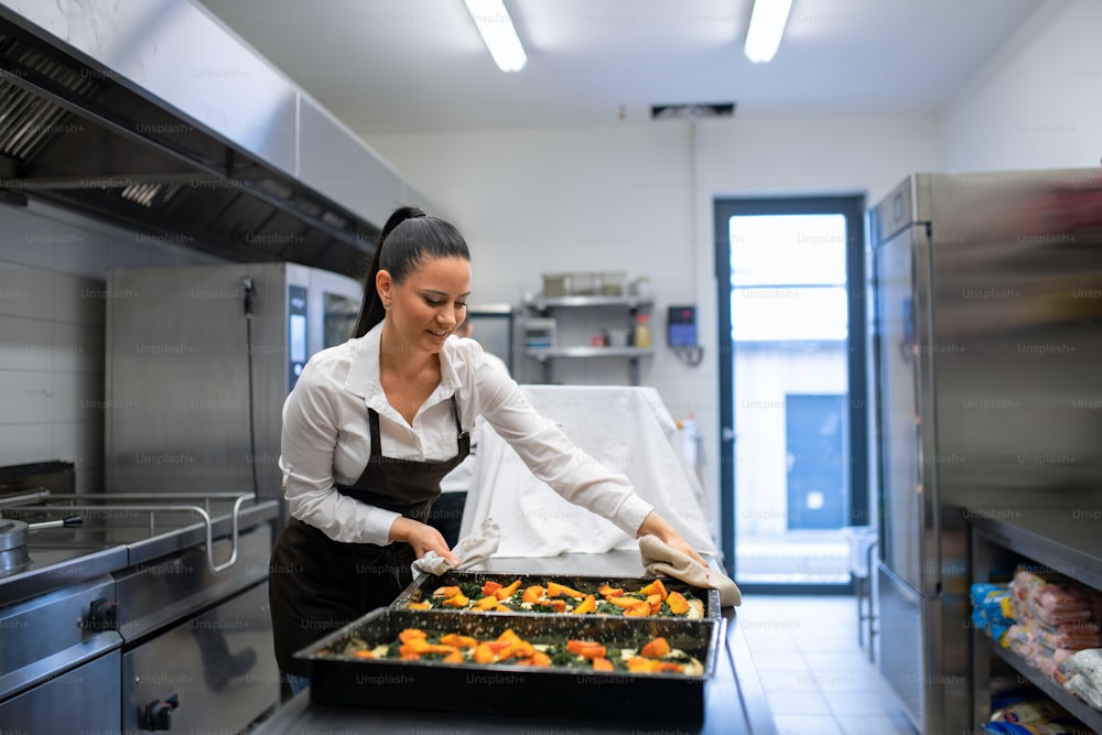 A professional chef working on her dishes indoors in restaurant kitchen.