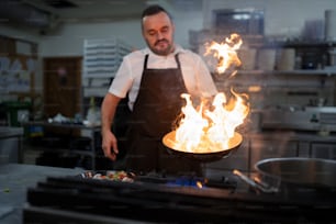 A professional chef preparing meal, flambing indoors in restaurant kitchen.
