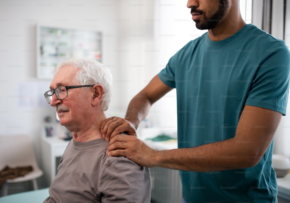 Un jeune kinésithérapeute masse le cou d’un patient âgé dans une salle de physique