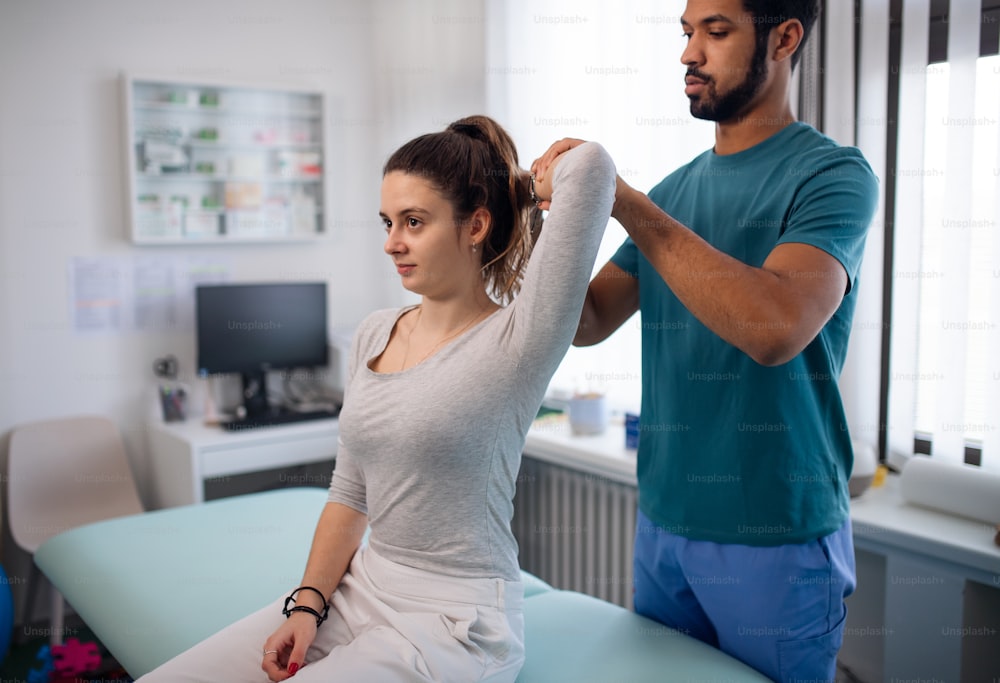 A young male physiotherapist examining young woman patient in a physic room