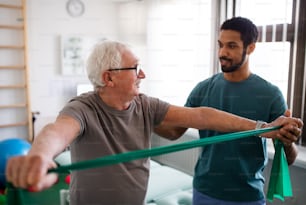Ein junger Physiotherapeut trainiert mit einem älteren Patienten in einem Physikraum