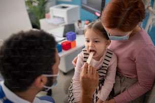 A zoung male doctor checking little girl's throat in his office.