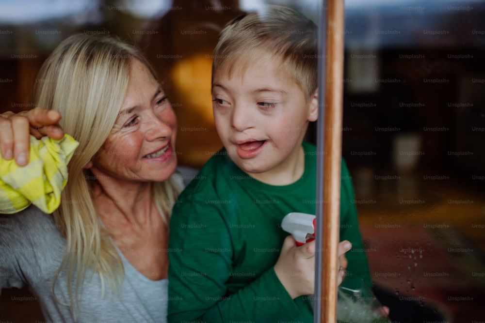 Ein Junge mit Down-Syndrom mit seiner Großmutter putzt Fenster zu Hause.