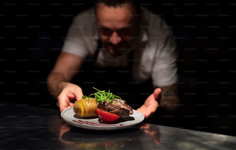 A chef handing plate with meal through order station in the commercial kitchen on black background.