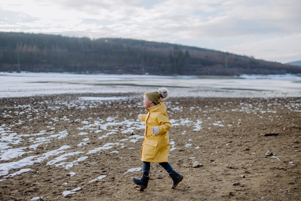 A happy little boy with Down running outside by lake in winter.