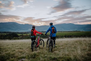 Eine Rückansicht von älteren Bikern, die im Herbst im Wald gehen und E-Bikes schieben.