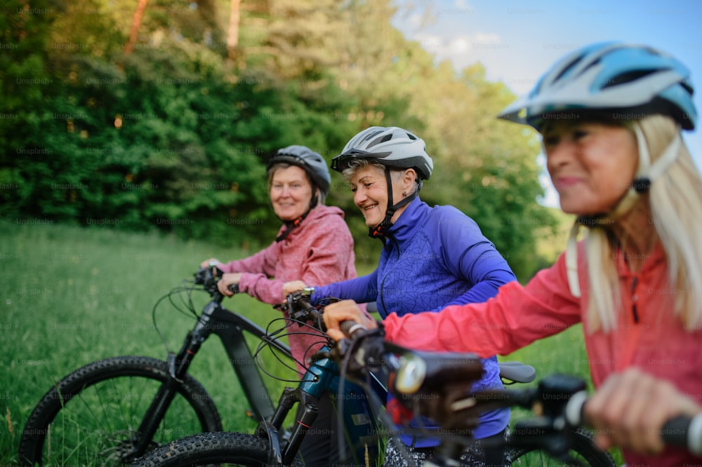 Happy active senior women friends pushing bicycles together outdoors in the nature.
