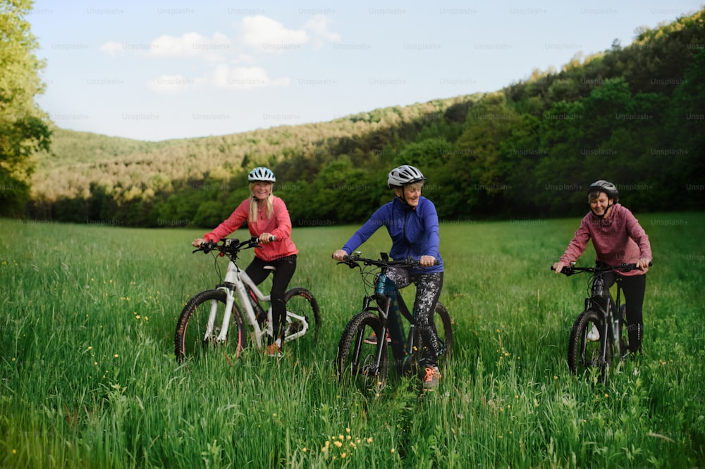 Happy active senior women friends cycling together outdoors in nature in meadow.Happy active senior women friends cycling together outdoors in nature in meadow.