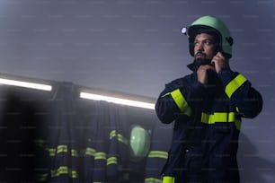 A low angle view of young African-American firefighter putting on helmet in fire station at night.