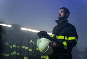 若いアフリカ系アメリカ人の消防士が夜の消防署で行動の準備をしているローアングルビュー。