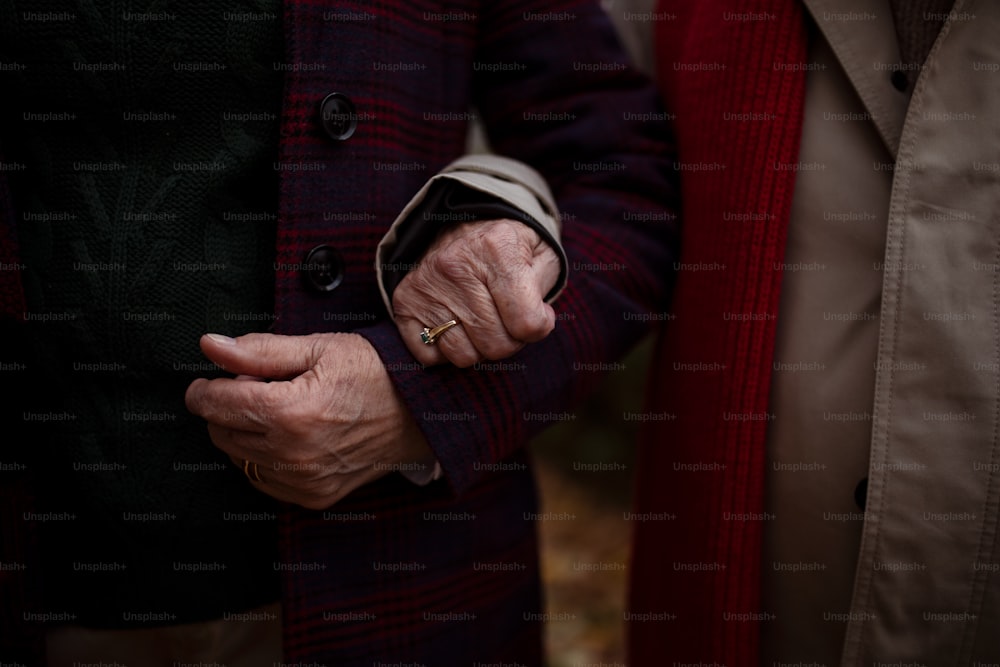 Un primo piano delle mani di una coppia anziana che si tiene durante una passeggiata all'aperto in città in autunno.