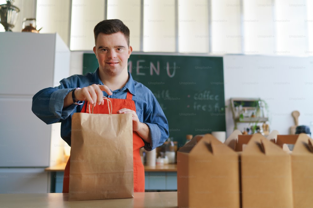 A cheerful young Down Syndrome waiter working in take away restaurant, social inclusion concept.