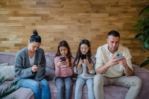 A family with two little daughters, everyone is using mobile phone in the living room.
