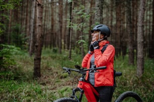 Una motociclista anziana che indossa il casco da ciclismo all'aperto nella foresta in un giorno d'autunno.