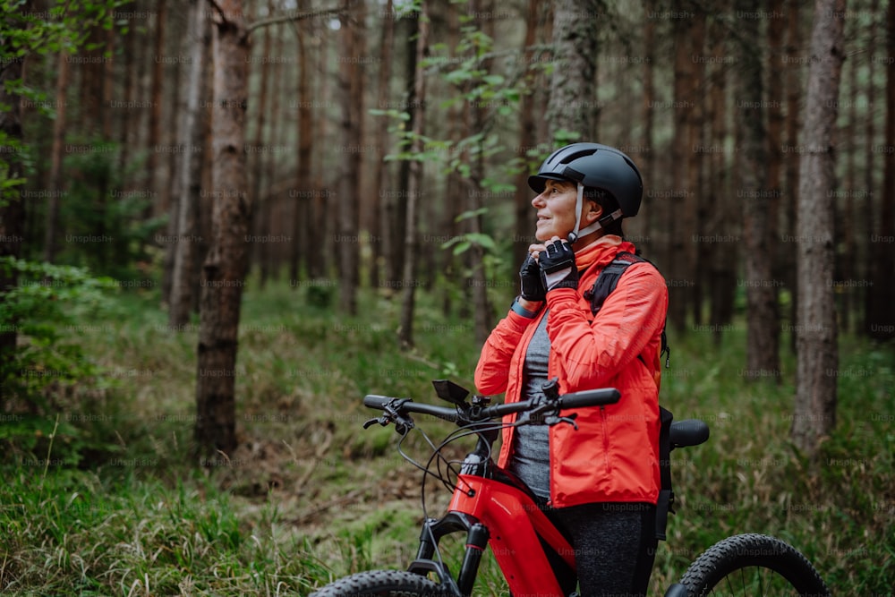 A senior woman biker putting on cycling helmet outdoors in forest in autumn day.