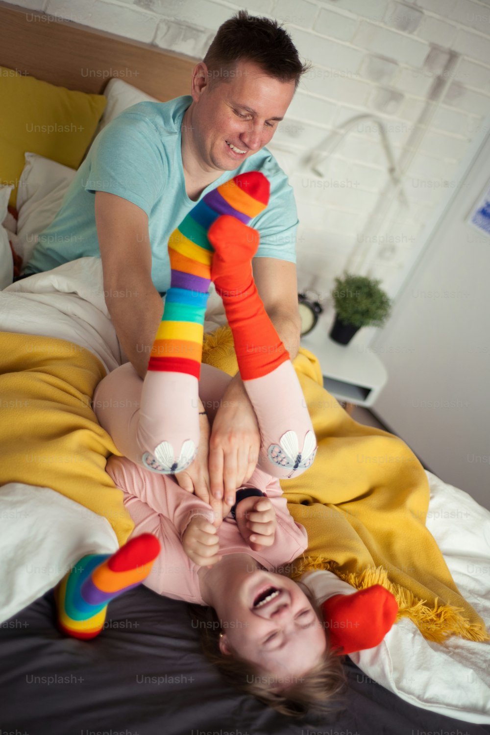 uma garotinha alegre com síndrome de Down deitada na cama e rindo quando seu pai está fazendo cócegas nela.