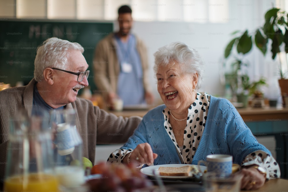 老人ホームの介護施設で朝食を楽しむ笑顔の高齢女性と男性。
