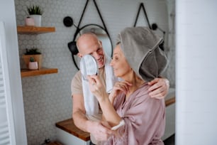 A senior couple in love in bathroom, looking at mirror and smiling, morning routine concept.