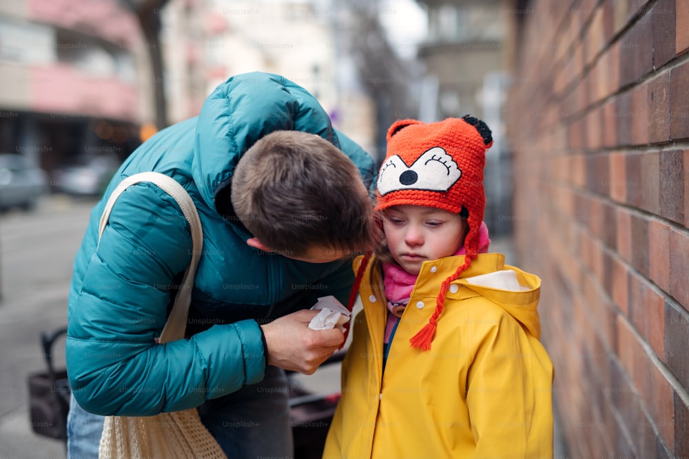 Ein Vater mit seiner kleinen Tochter mit Down-Syndrom auf einem Spaziergang in der Stadt im Winter.