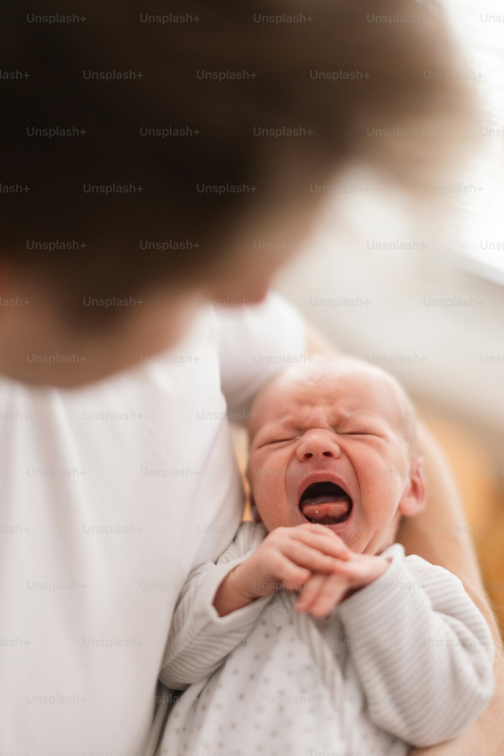 A father holding his crying newborn son at home.