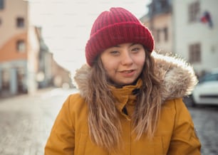 A happy young woman with Down syndrome weraing parka and hat, walking in town and looking at camera.
