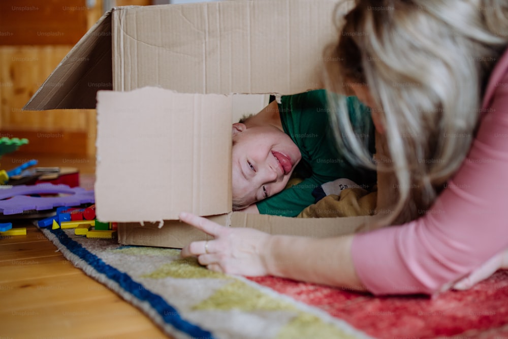 A boy with Down syndrome with his mother playing with box together at home.