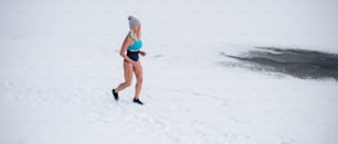Mulher sênior ativa feliz em maiô correndo ao ar livre no inverno, conceito de terapia fria.