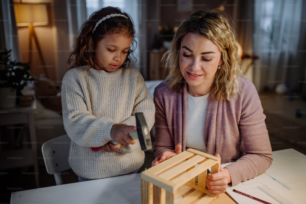 Una niña feliz renovando una caja de madera junto con su madre en casa.