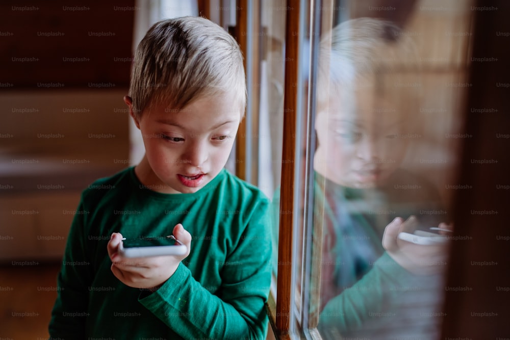 A sad little boy with Down syndrome using smartphone at home