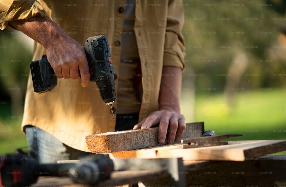 Un gros plan d’un charpentier bricoleur travaillant dans un atelier de bricolage de menuiserie à l’extérieur avec une perceuse.