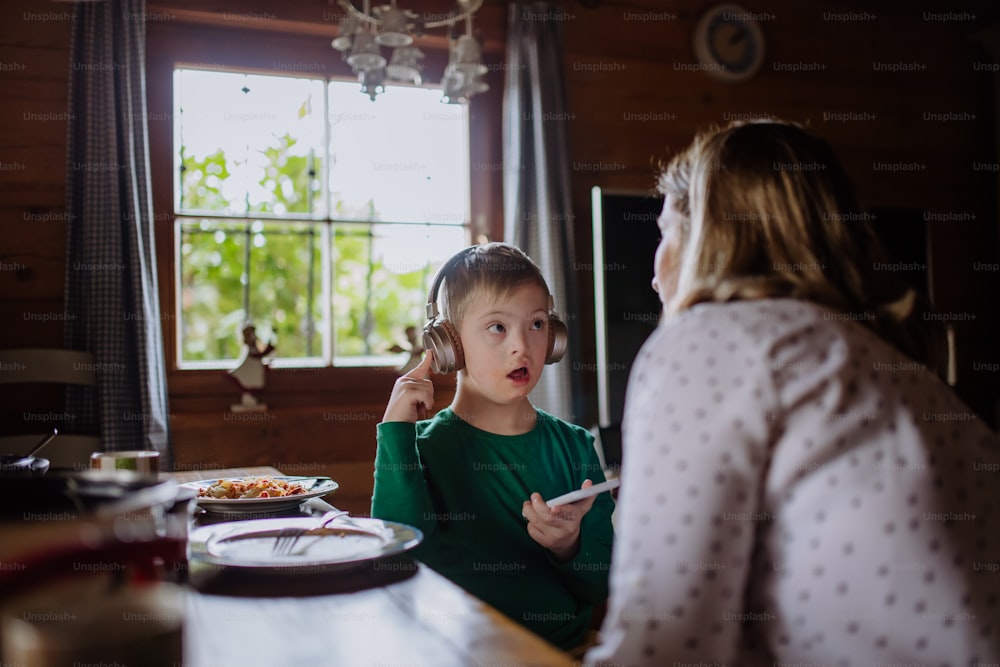 A boy with Down syndrome with his mother having lunch and using smartphone at home