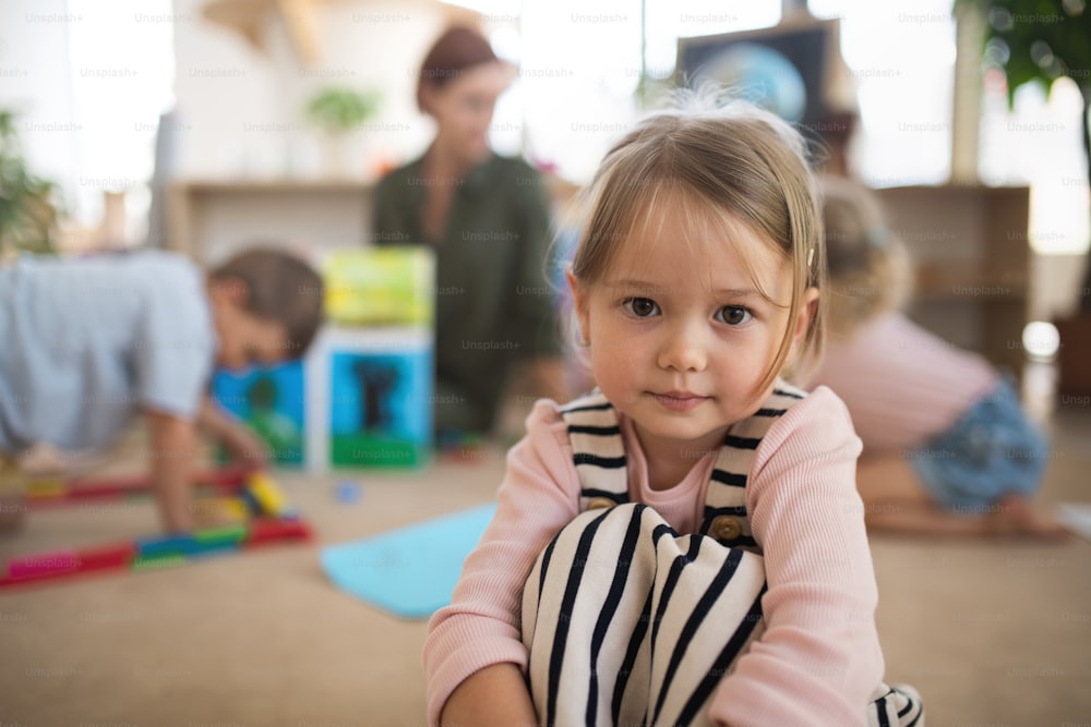 A portrait of small nursery school girl indoors in classroom, looking at camera.