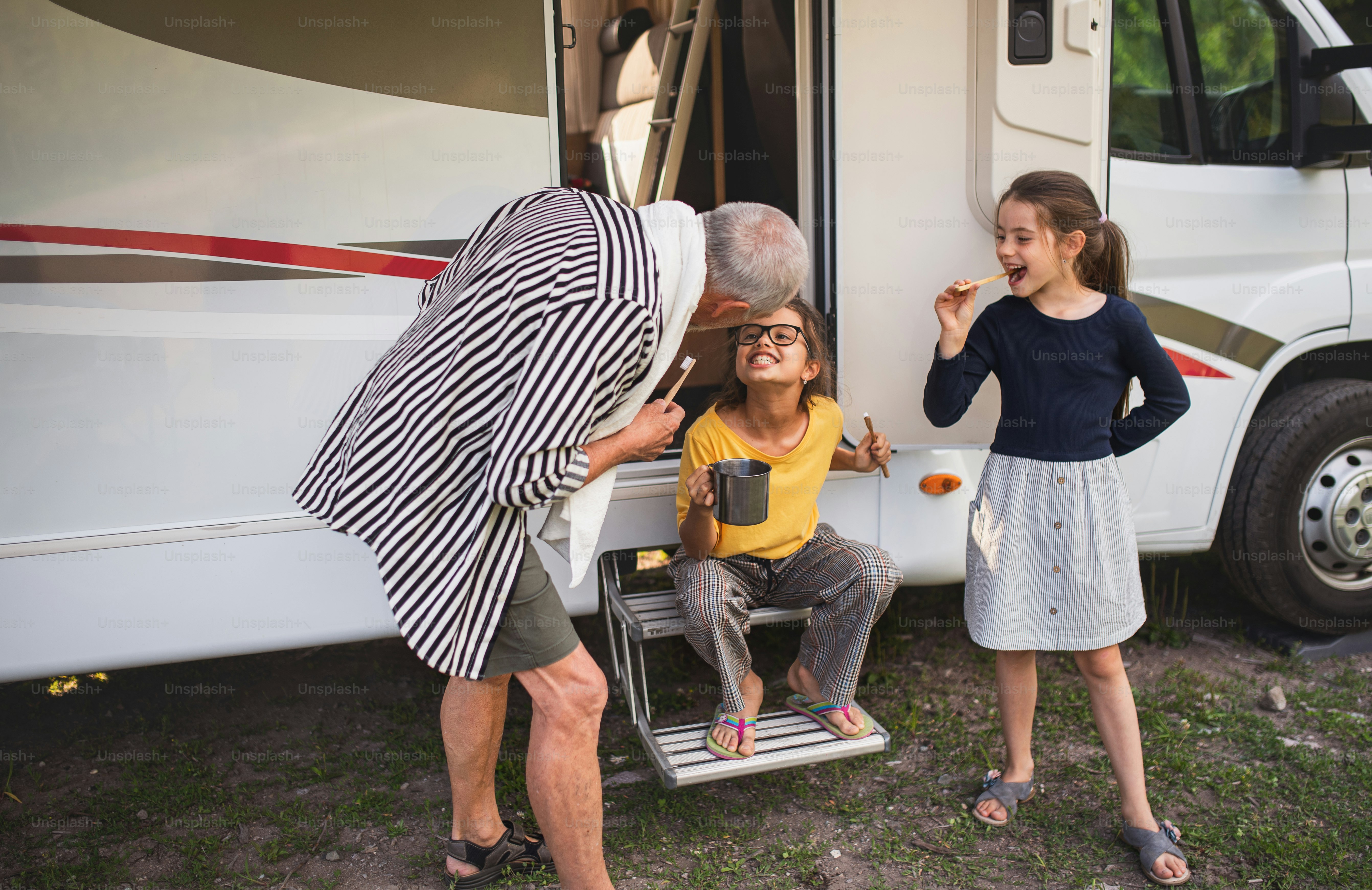 Niñas pequeñas felices con un abuelo cepillándose los dientes en caravana, viaje de vacaciones en familia.