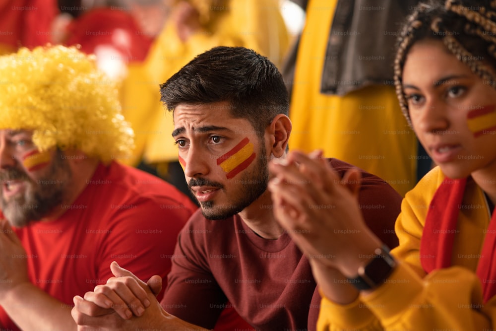 Worried football fans supproting a spanish national team in live soccer match at stadium.